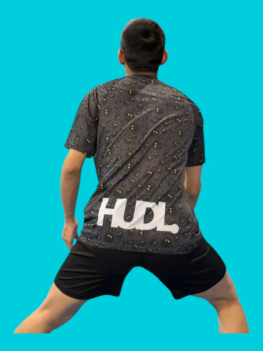 A man with his back turned wearing a HUDL Rally in Motion limited edition squash tee – XTPro performance fabric, unique graphic design black with white squash balls 