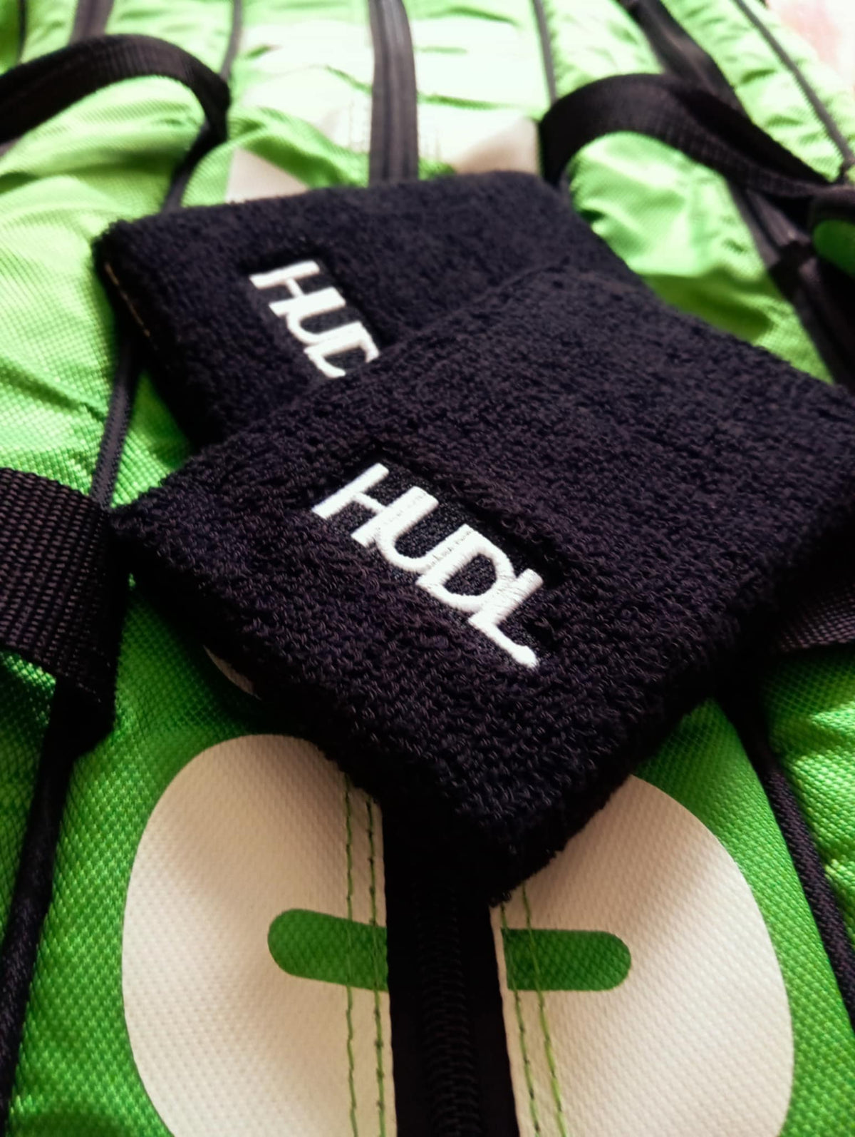 HUDL squash wristbands long two-pack – absorbent sweat bands for squash court performance with the HUDL logo, placed on a green squash bag 